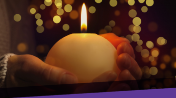 hands holding candle with holiday lights in background