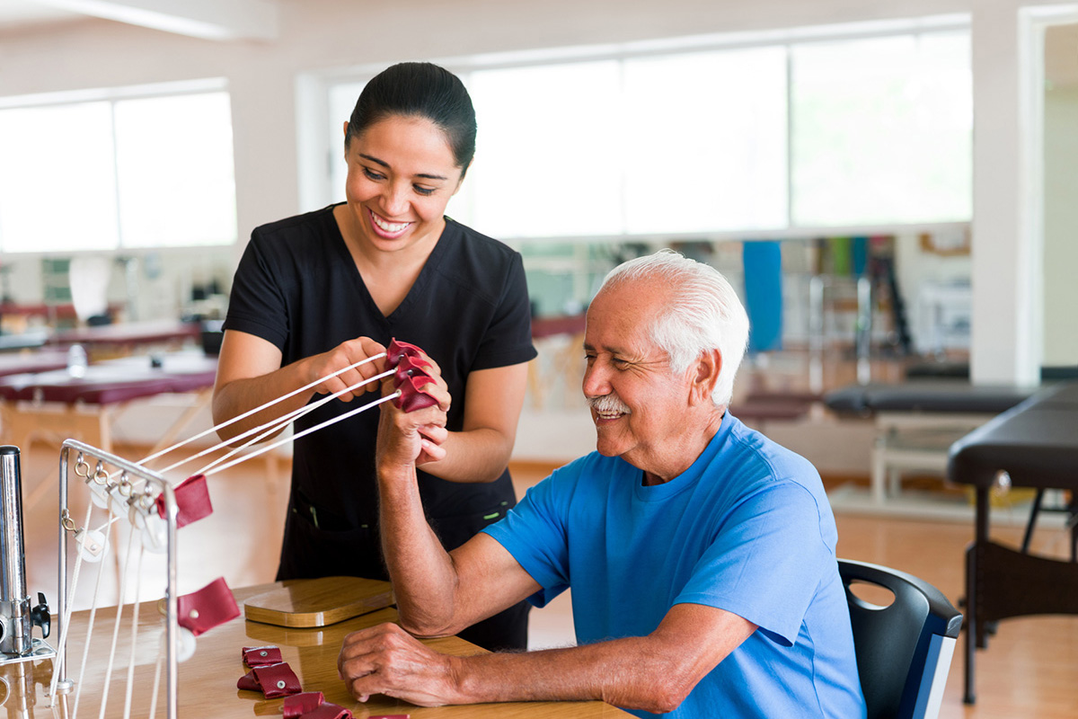 older man doing hand therapy exercises while seated at a table